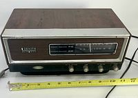 Front view showing brand badge, dial scale and control knobs with measuring tape for width reference