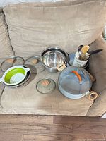 All items grouped on sofa: pot with lid, bowls, lids, colander, utensil holder with utensils