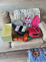 Overview of lot on couch showing grill, storage cube, tie-dye kits, bowls, pumpkins, tumblers, trays, blankets