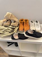 All footwear pairs on shelf: tan fur boots, rust ankle boots, white sneakers, black slip-ons