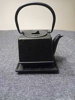 front view of square cast iron teapot on trivet