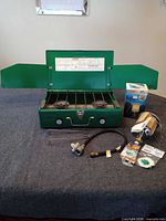 Stove open showing burners, grate, wind guards, regulator hose, lantern box, tool, spare parts