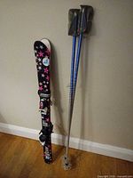 Full view of skis and poles standing against wall