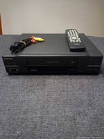 Front view of Toshiba VCR with remote and RCA cable on top