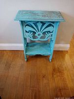 full front view of turquoise distressed wood plant stand showing carved panels and lower shelf
