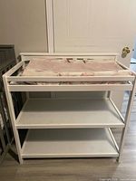 Front view of white wooden changing table with pad on top and two open shelves
