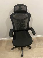 Front view of black mesh ergonomic office chair with armrests and headrest
