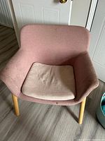 Front view of pink accent chair showing curved back, arms, beige cushion and wood legs
