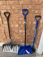 All three snow shovels standing against brick wall