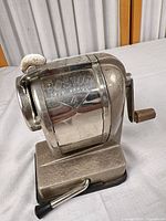 Front and side view of Boston Self Feeder 4 sharpener showing brand name, crank handle, suction base