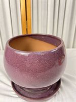 Front view of purple glazed planter on saucer showing overall shape and glaze, drainage hole visible