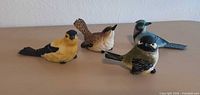 Four assorted resin bird figurines displayed side by side
