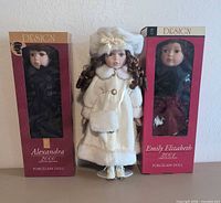 All three Design porcelain dolls: two boxed (Alexandra 2000, Emily Elizabeth 900) and one unboxed in white coat