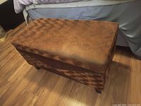 Closed brown upholstered hope chest on wooden floor