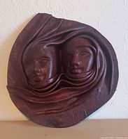 Front view of sculpted leather mask showing twin faces and signature