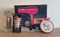 All four items: boxed Conair hair dryer, packaged foot rasp, sealed Fing’rs press-on nails, cross-stitch hoop