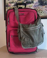 Front view of red suitcase with green crossbody bag draped over handle