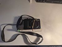 Front view of Canon PowerShot G9 camera with strap resting on folded manual