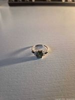 Front view showing emerald-cut green center stone and side accent stones