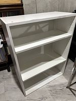 Front view of white shelving unit showing three shelves and adjustable peg holes
