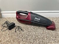 Left side view of Shark red/black 15.6V handheld vacuum beside charger