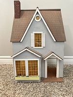 Front view of grey wooden dollhouse with bay window, planter, porch and chimney