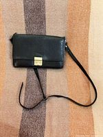Front view of black leather clutch with strap and gold-tone clasp