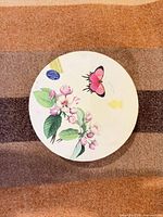 Round decorative box lid displaying floral and butterfly graphics