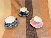 Three porcelain teacup and saucer sets displayed upright on fabric background