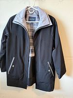 Front view of dark navy Nautica jacket showing zip front, two zip pockets with snap closures, light grey collar lining and plaid interior
