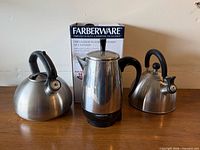 Front view of Farberware percolator flanked by two stainless steel kettles, box visible behind