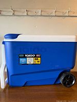Left side view of blue Igloo 38qt rolling cooler showing handle and wheel