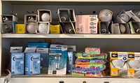 Overview upper and lower shelves showing assorted loose bulbs in sleeves, boxed bulbs, packaged LED and incandescent bulbs, sponge packs