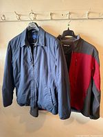 Front view of both jackets hanging: navy zip jacket left, Kirkland softshell right