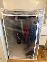 Full view of metal garment rack inside transparent vinyl cover with white trim and zipper