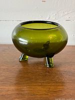 Olive green three-footed glass bowl on wood surface