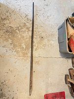 Full view of steel fencing spud bar lying on floor, showing pointed and chisel ends