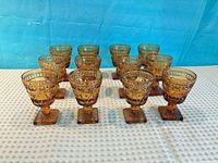 Front view of all 12 amber pressed glass goblets with square bases
