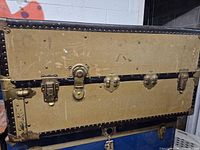 Front view showing tan canvas panels, three brass latches, lock plate, black band, riveted trim
