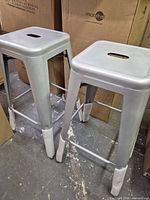 Two metal bar stools standing side by side showing full form and protective foam on legs