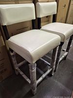 Two white faux leather counter stools assembled, packaging on legs