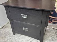 Front view of dark two-drawer chest showing metal handles and curved side detail