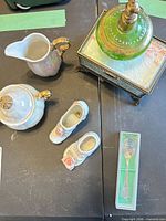 Overall view showing porcelain creamer and sugar, shoe figurines, green perfume bottle, trinket box, boxed spoon