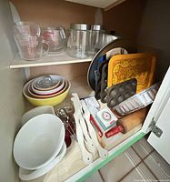 Cabinet view showing Pyrex cups, glass pitchers, pizza pan, mixing bowls, white bowls, utensils