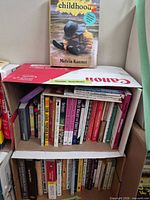 Two cartons stacked as shelves holding assorted books; Childhood by Melvin Konner displayed on top