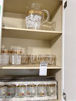 Cabinet view showing glass pitcher on top shelf, tumblers on middle shelf, boxed juice glasses on lower shelf