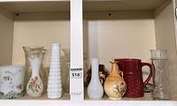Cabinet shelf showing assortment of nine glass and ceramic vases