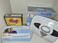 Group shot showing Hairmax laser device box, HoMedics ParaSpa Plus paraffin bath box, HoMedics white foot massager, and boxed wooden roller foot massager