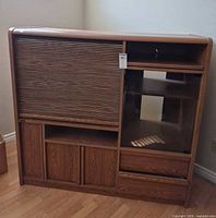 Front view of wood entertainment center showing tambour door closed, glass panel, lower cabinets and casters