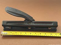 Top view of black ACCO 3-hole punch beside tape showing roughly 12 in length